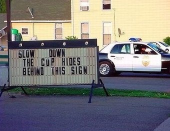 custom_1257994914480_slow-down-cop-hides-behind-sign